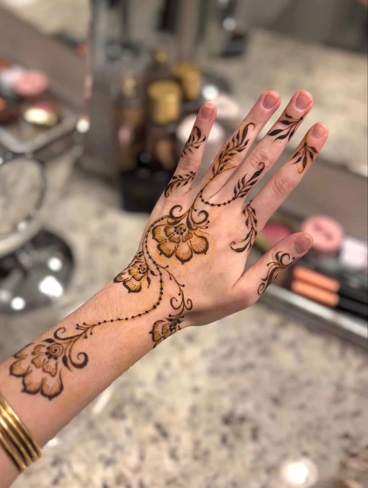 Detailed brown henna with flowers and trailing vines from fingers down the wrist
